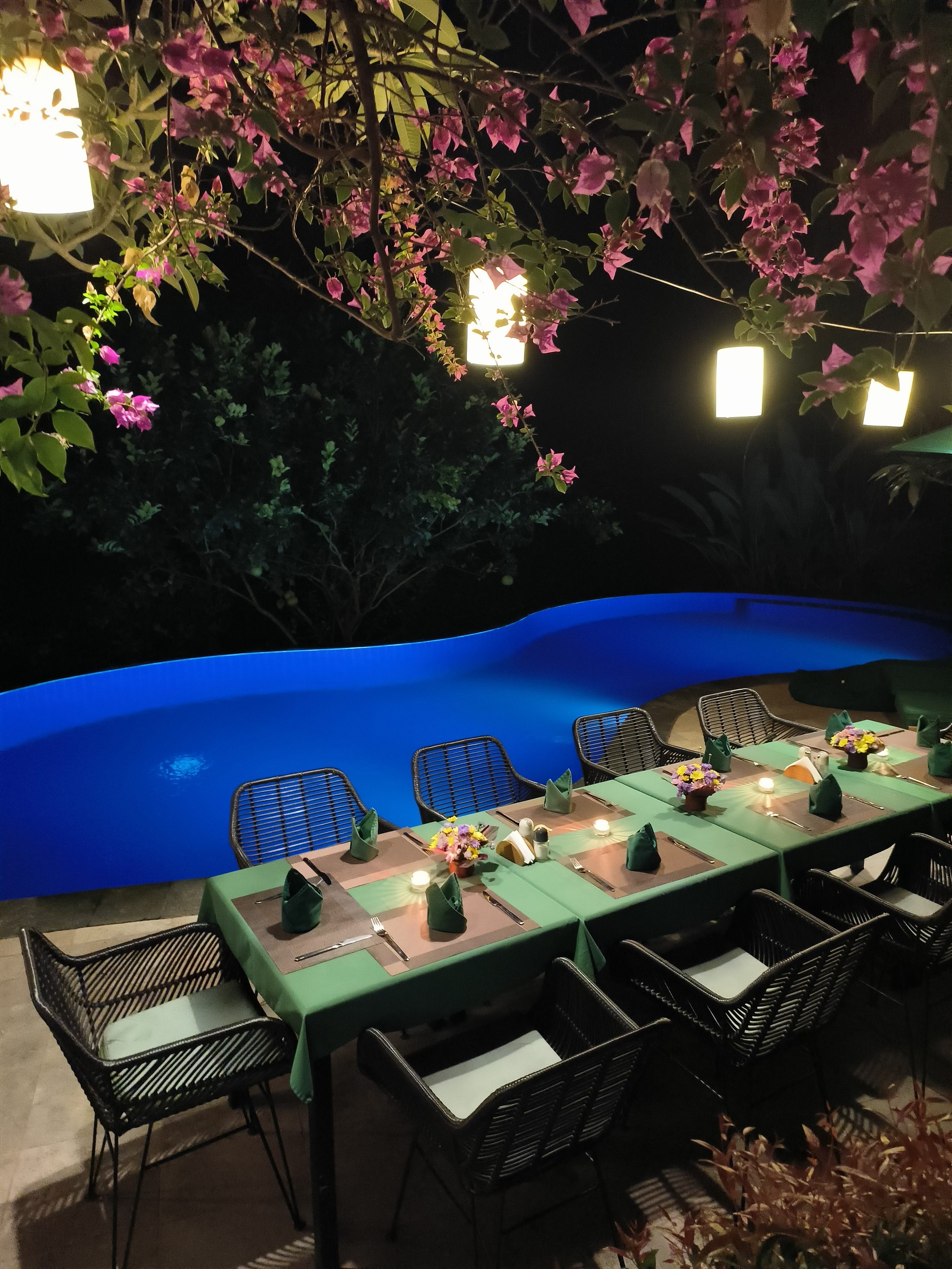 Long dining table lit by lanterns beside the Alamanda pool after dark